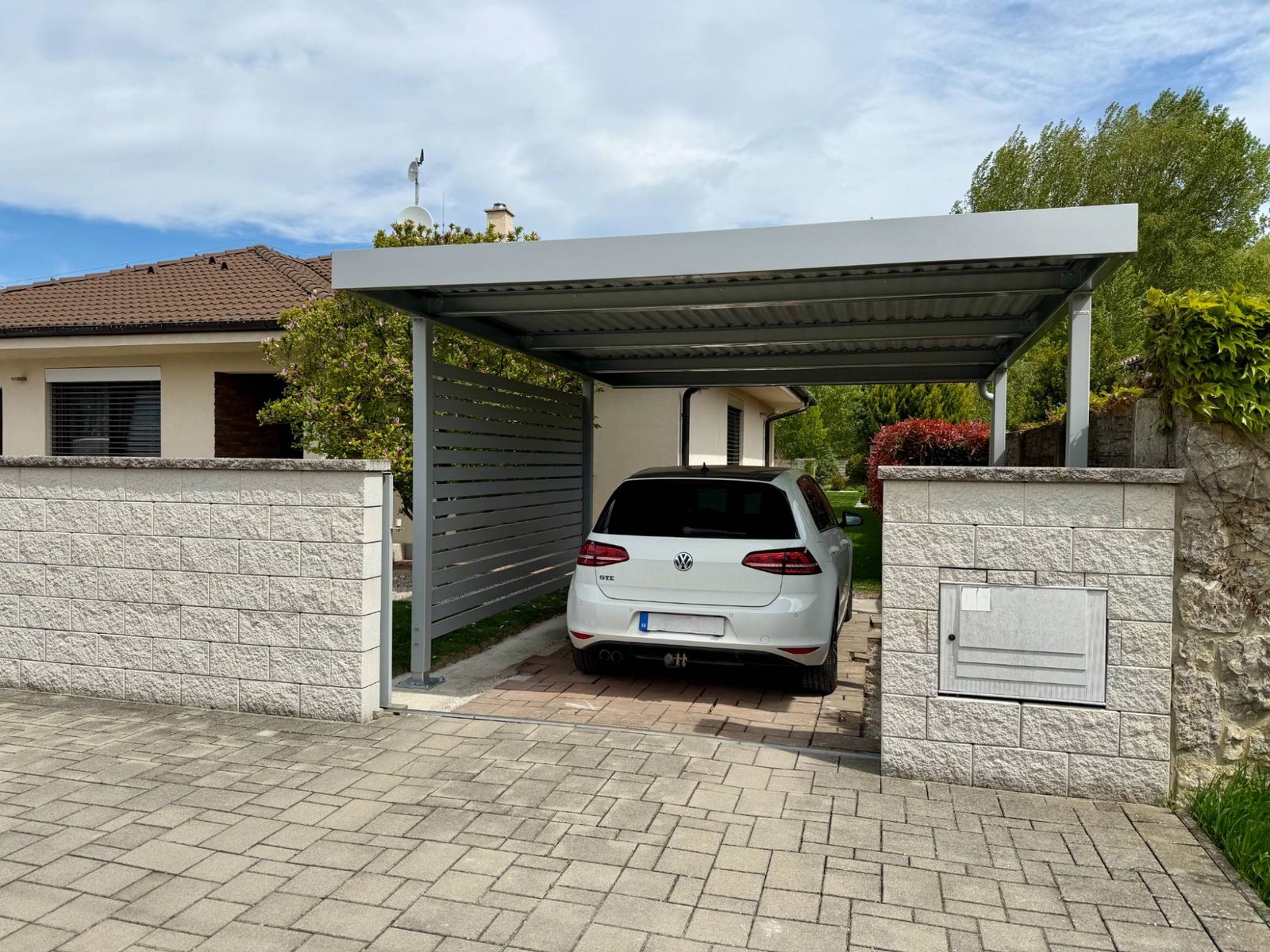Oceľový prístrešok Koverta so svetlou strechou a lamelovou bočnou stenou, pod ním zaparkované auto