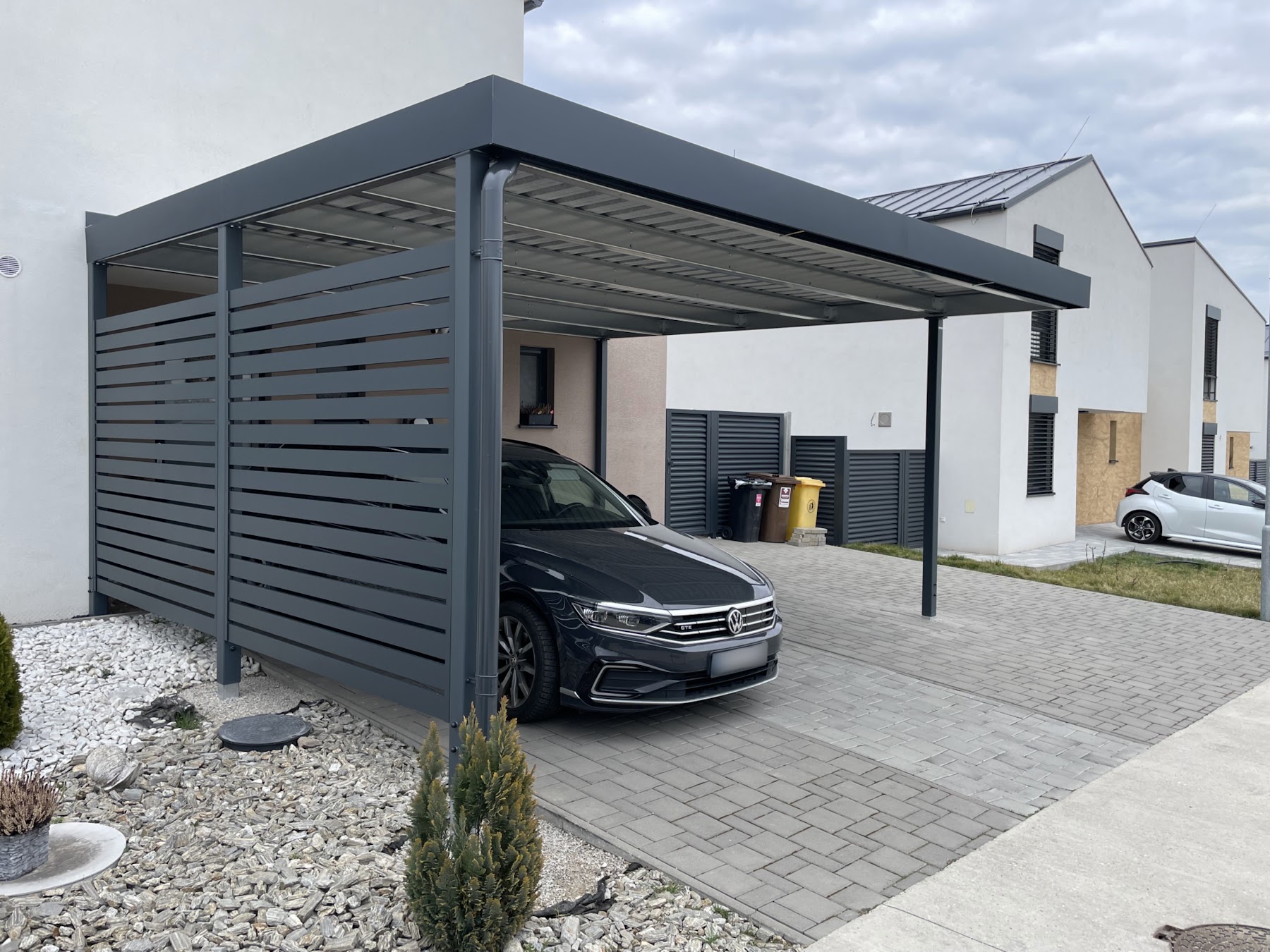 Čierne auto pod oceľovým prístreškom Koverta pri rodinnom dome